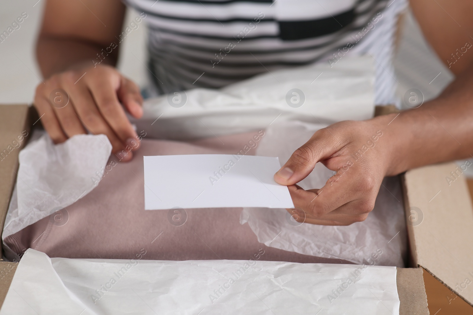 Photo of Young man holding greeting card near parcel with Christmas gift, closeup