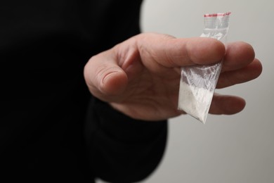 Photo of Drug addiction. Man with plastic bag of cocaine on light grey background, closeup