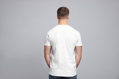 Man wearing white t-shirt on light grey background, back view. Mockup for design