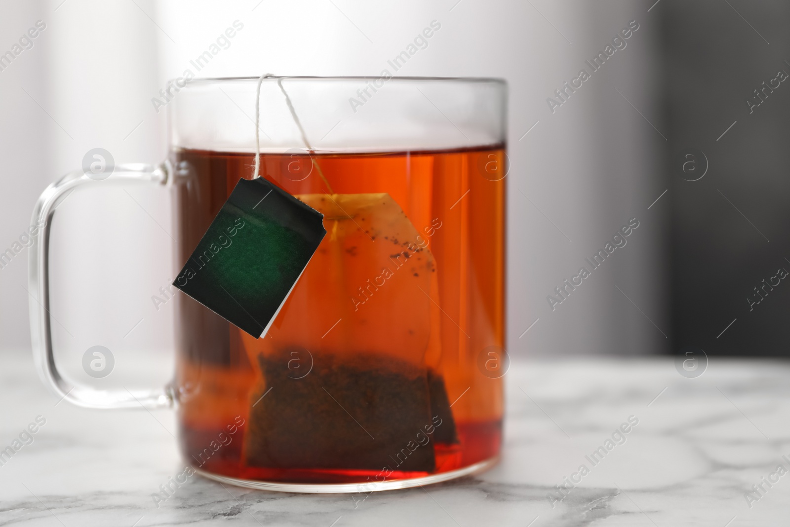 Photo of Tea bag in cup of hot water on white marble table