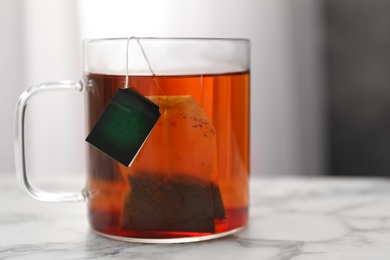 Tea bag in cup of hot water on white marble table