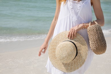 Photo of Woman with beach bag and straw hat near sea, closeup