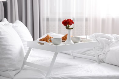 Photo of Tray with tasty breakfast and flowers on bed at home