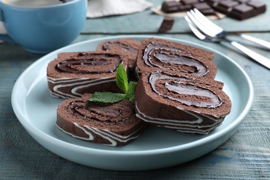 Photo of Tasty chocolate cake roll with cream and mint on blue wooden table, closeup