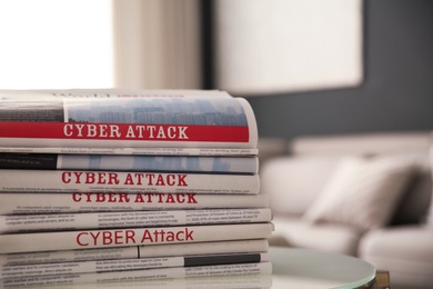 Photo of Stack of newspapers with headlines CYBER ATTACK on table indoors, closeup