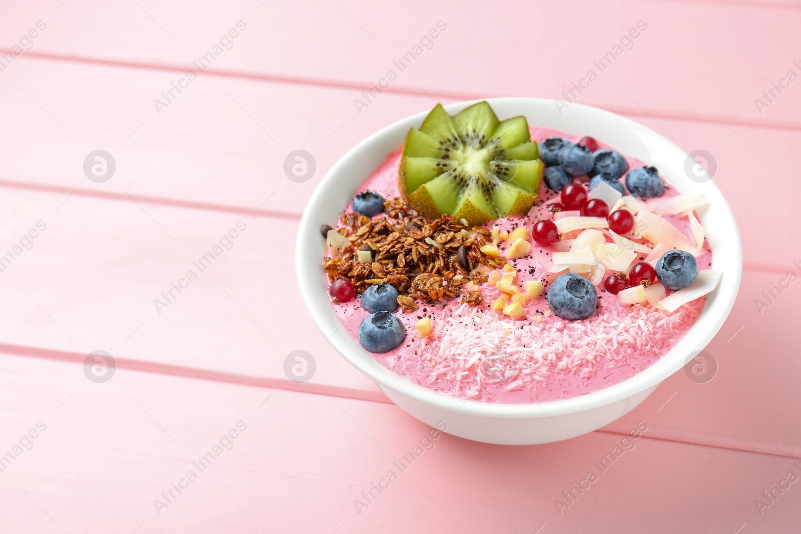 Photo of Tasty smoothie bowl with fresh kiwi fruit, berries and granola on pink wooden table, space for text