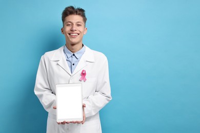 Photo of Mammologist with pink ribbon showing tablet on light blue background, space for text. Breast cancer awareness