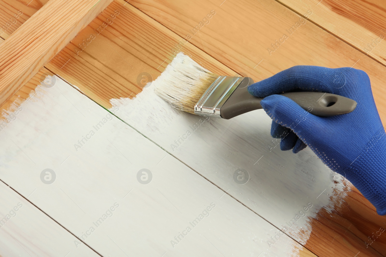Photo of Worker applying white paint onto wooden surface, above view. Space for text