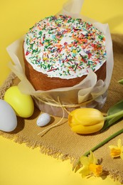 Photo of Traditional Easter cake with sprinkles, decorated eggs and flowers on yellow background