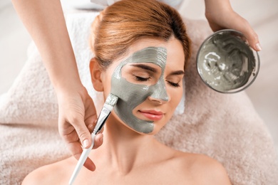 Photo of Cosmetologist applying mask onto woman's face in spa salon, top view