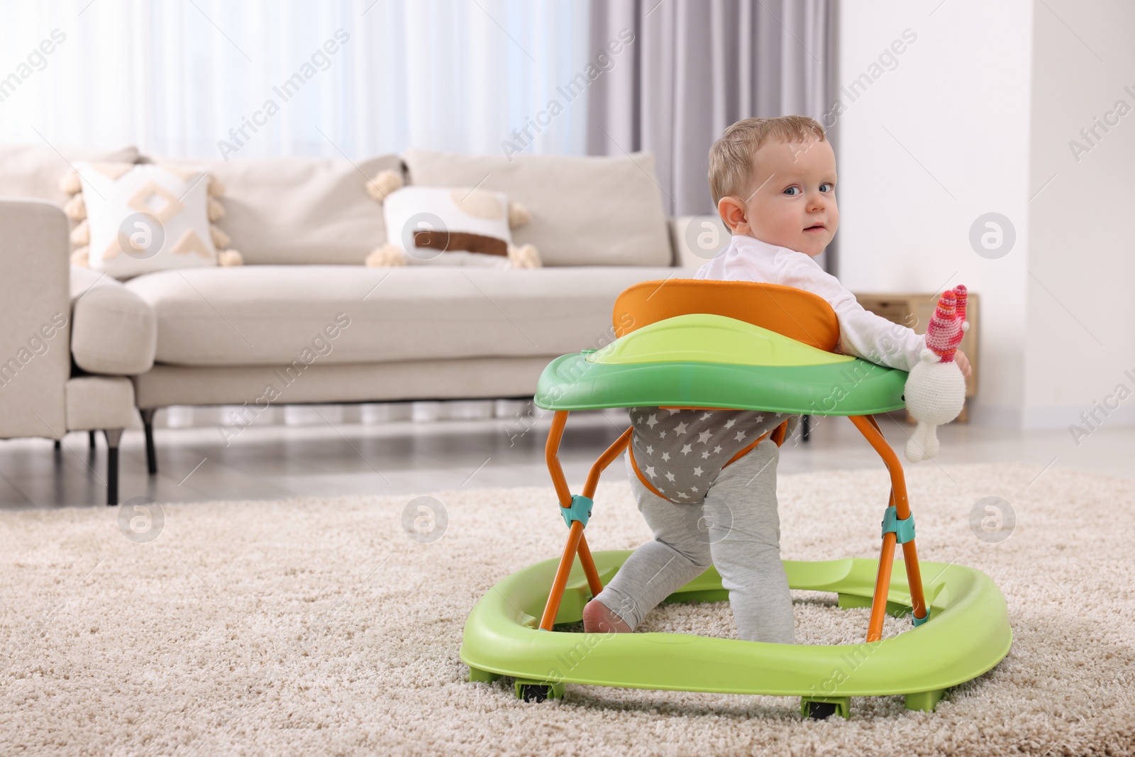 Photo of Cute baby making first steps with toy walker at home, space for text