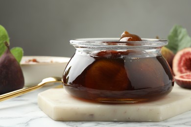 Photo of Jar of tasty sweet fig jam on white marble table, closeup