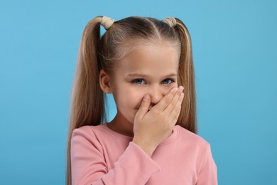 Photo of Embarrassed little girl covering her mouth with hand on light blue background