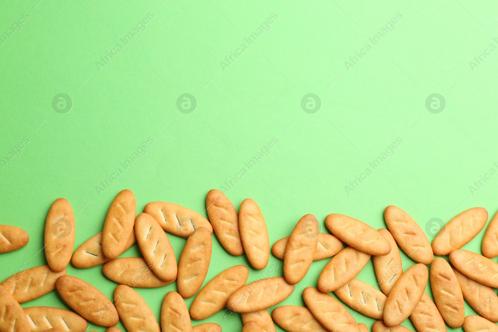 Photo of Delicious crackers on light green background, flat lay. Space for text