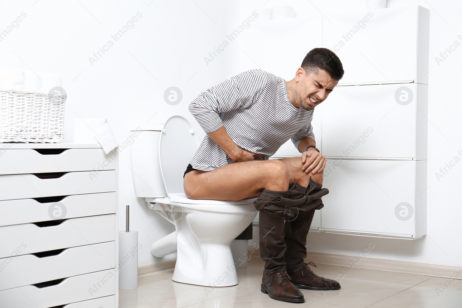 Photo of Man with stomach ache sitting on toilet bowl in bathroom