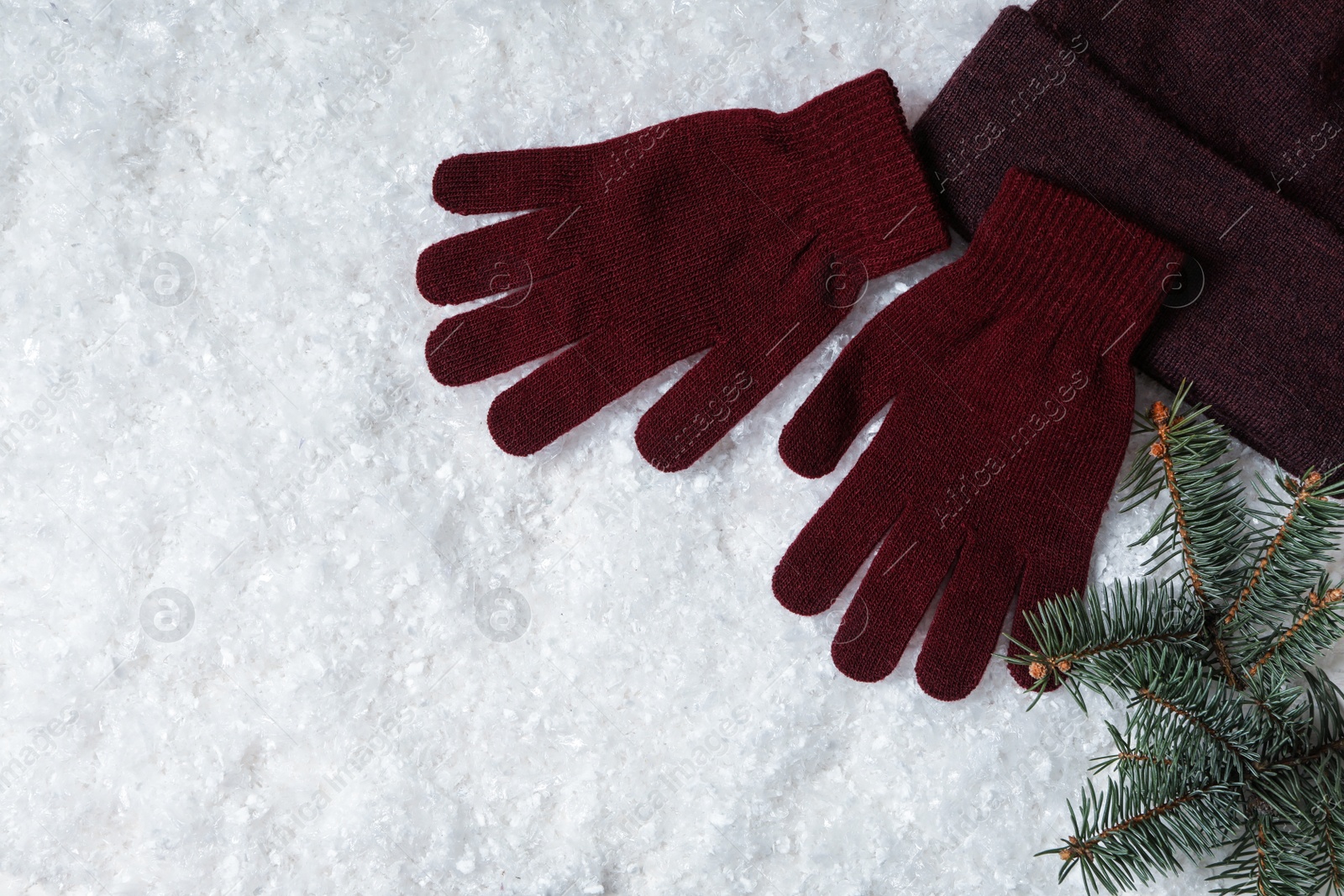 Photo of Stylish woolen gloves, hat and fir branches on artificial snow, flat lay. Space for text