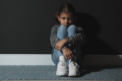 Sad little girl near black wall. Domestic violence concept