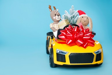 Child's electric car with toys, gift boxes and Christmas decor on light blue background, space for text