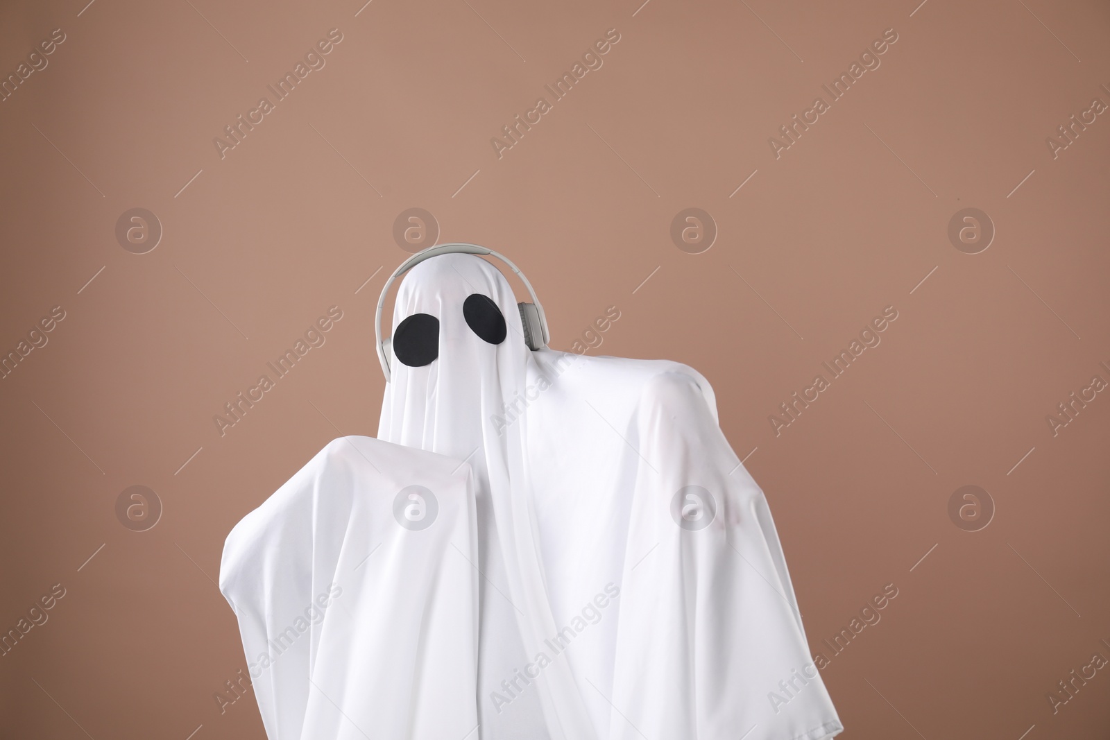 Photo of Person in ghost costume with headphones on dark beige background