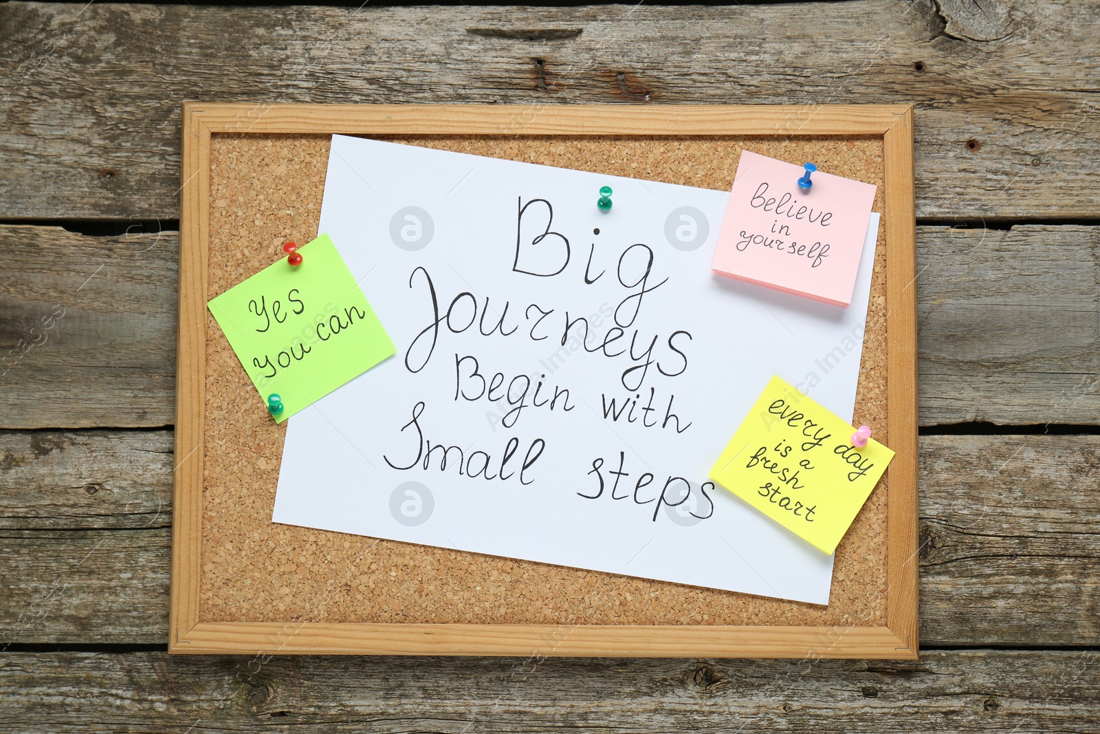 Photo of Corkboard with motivational quotes on wooden table, top view