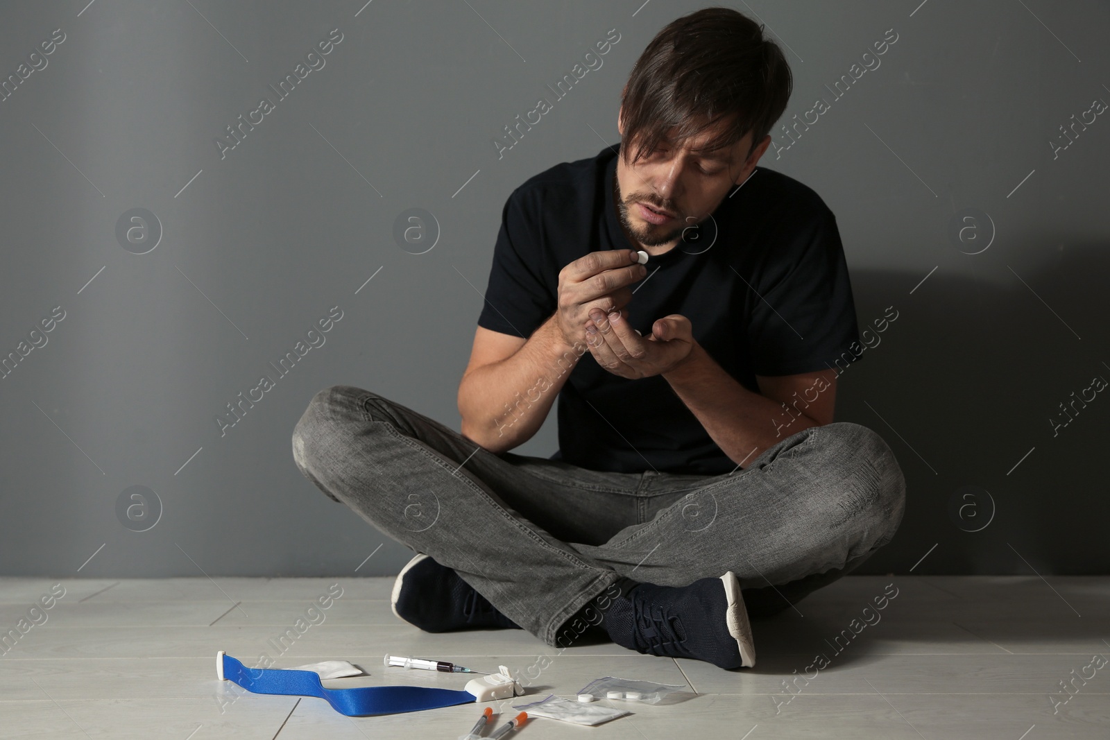 Photo of Young addicted man with drugs sitting near grey wall. Space for text