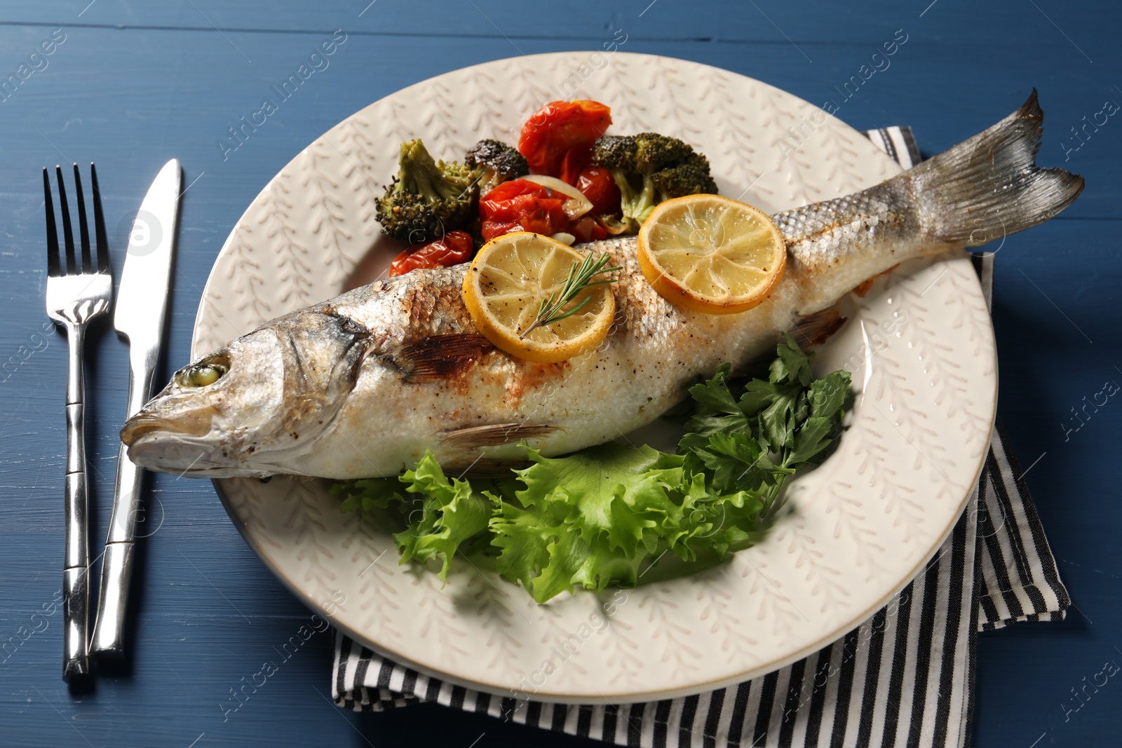 Photo of Delicious baked fish and vegetables served on blue wooden table