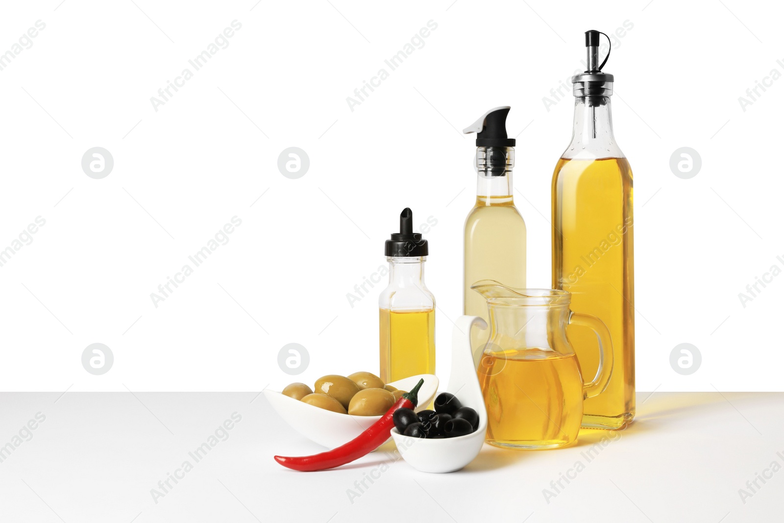 Photo of Bottles of different cooking oils, olives and chili pepper on white background, space for text