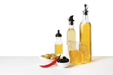 Photo of Bottles of different cooking oils, olives and chili pepper on white background, space for text