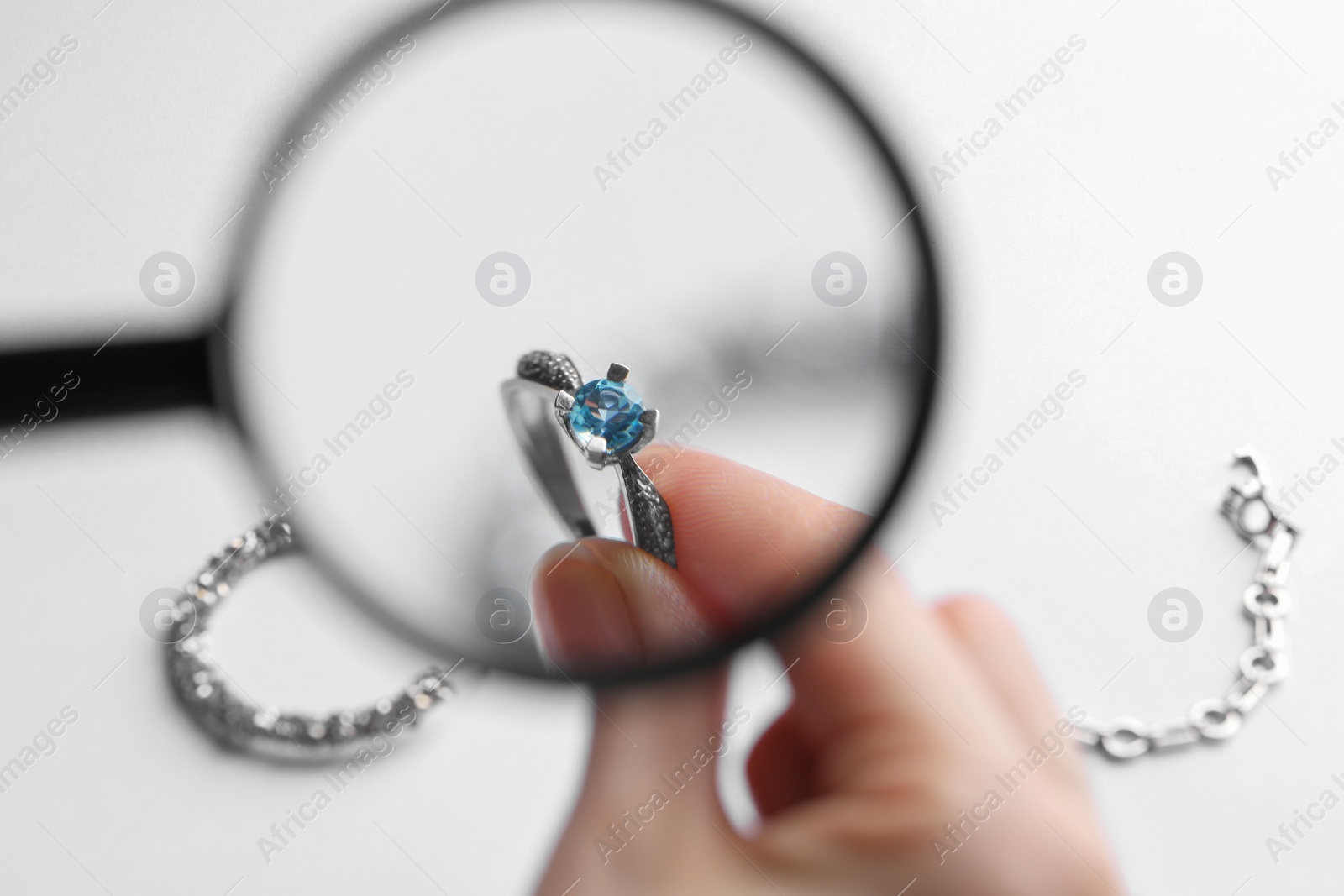 Photo of Jeweler examining topaz ring with magnifying glass at white table, closeup