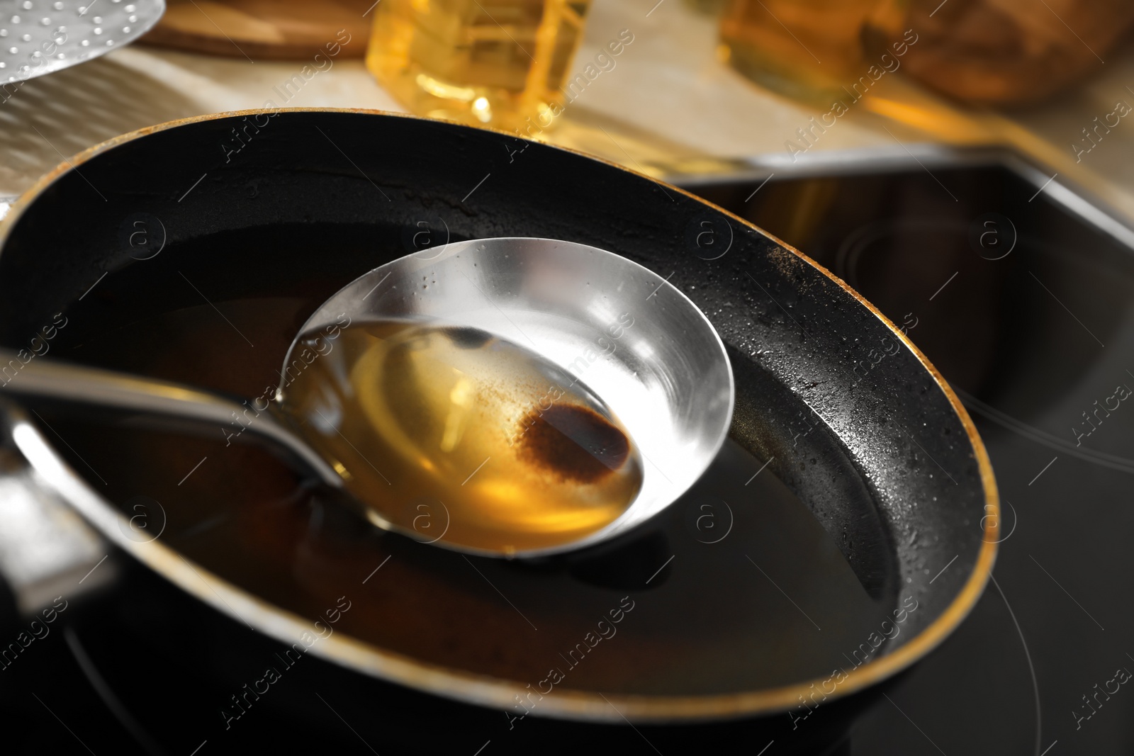 Photo of Frying pan and ladle with used cooking oil on stove, closeup