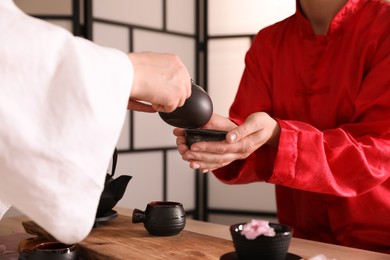 Master pouring freshly brewed tea into guest's cup during traditional ceremony at table, closeup