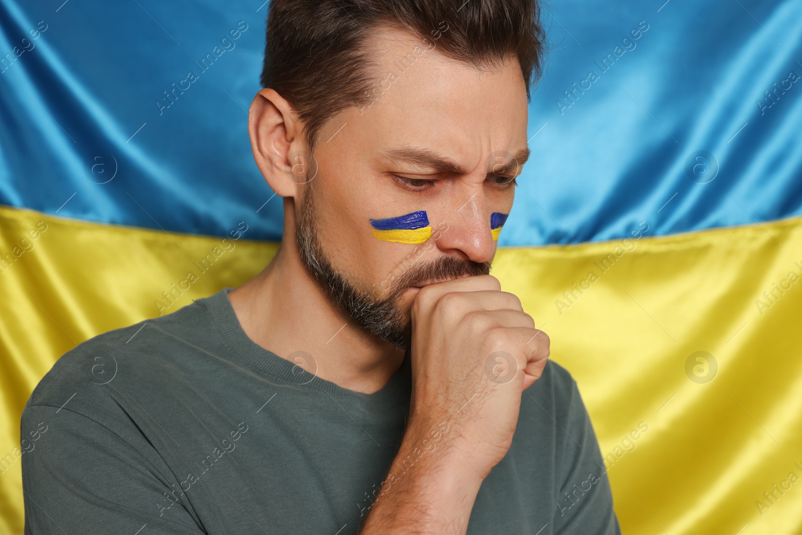 Photo of Sad man with face paint near Ukrainian flag