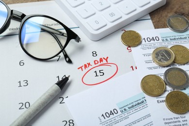 Photo of Calendar with date reminder about tax day, documents, pen, coins, glasses and calculator on table, closeup