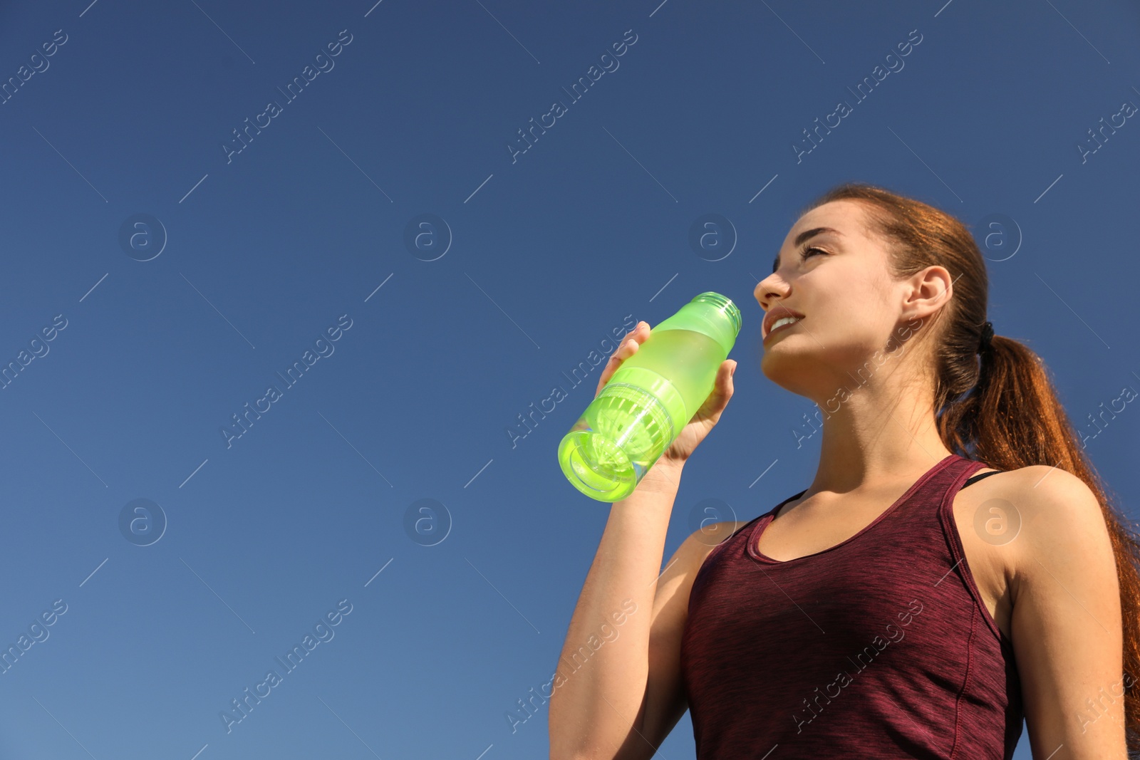 Photo of Young sporty woman drinking water from bottle against blue sky on sunny day