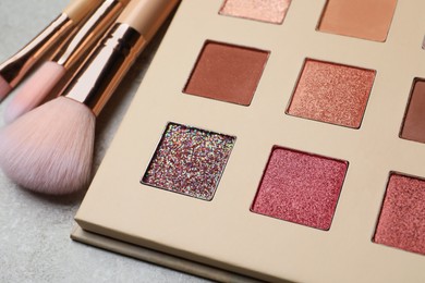 Beautiful eye shadow palette and brushes on grey table, closeup