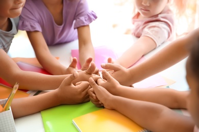 Little children putting their hands together at table, closeup. Unity concept