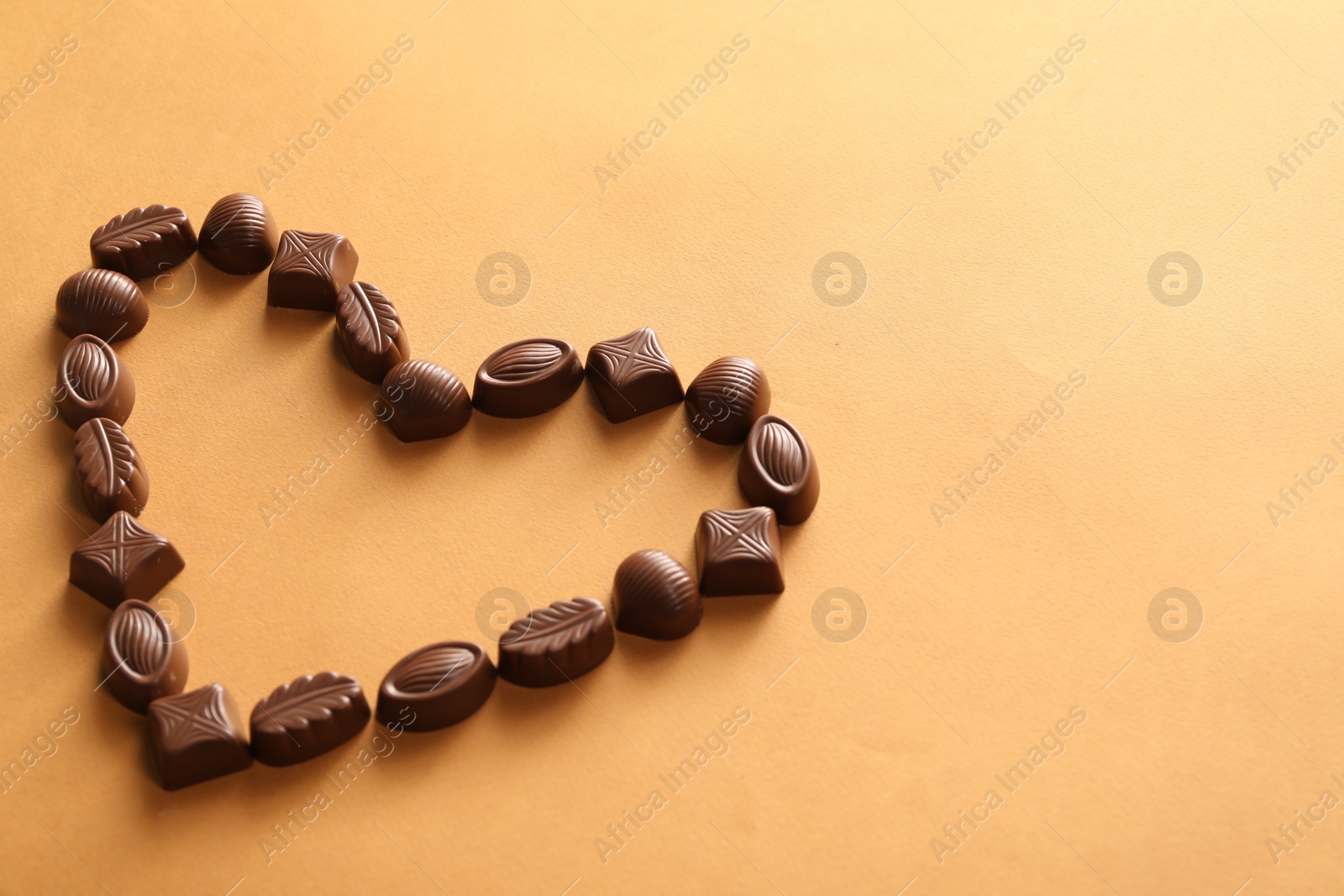 Photo of Heart made with delicious chocolate candies on brown background. Space for text