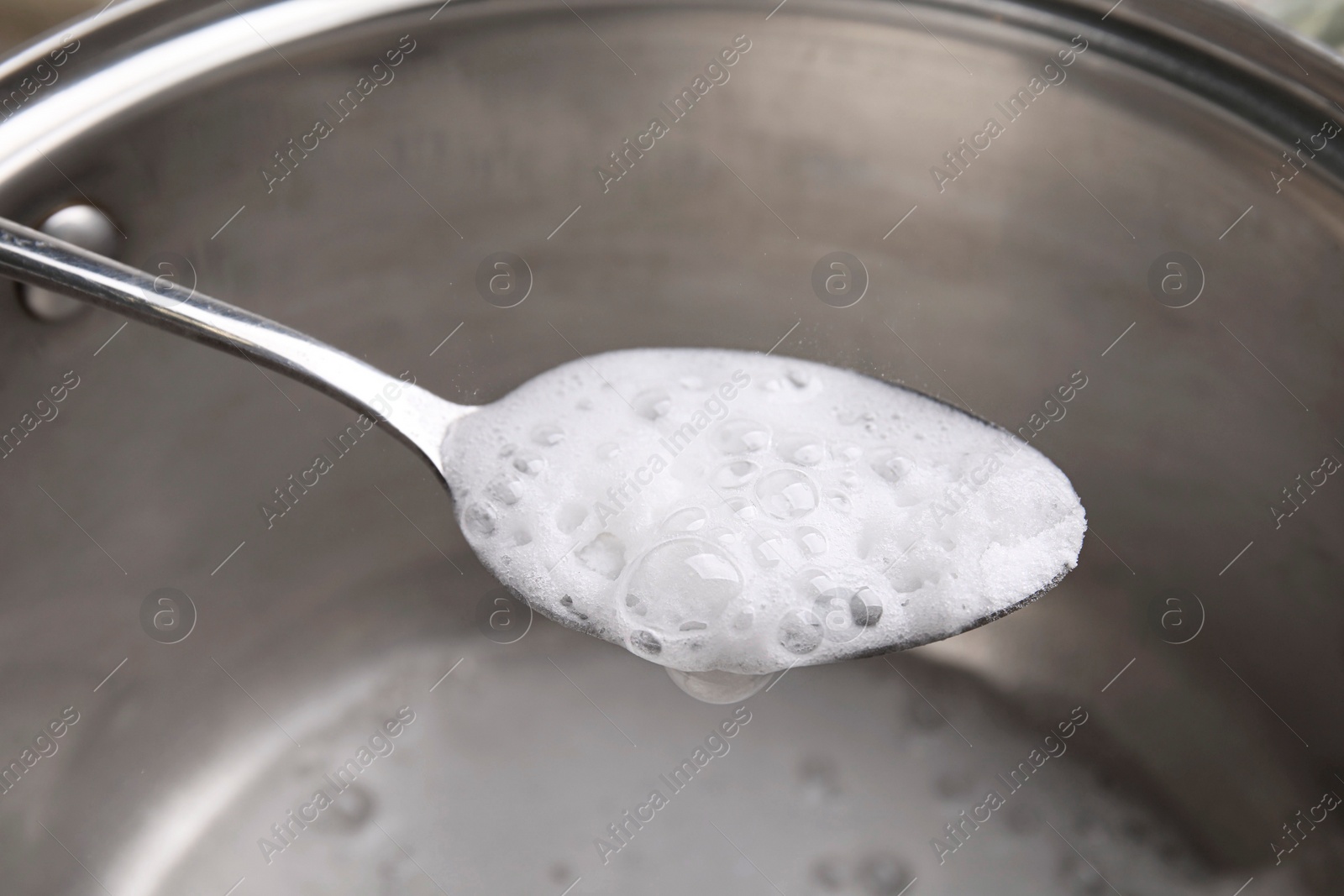 Photo of Chemical reaction of vinegar and baking soda in spoon over saucepan, closeup