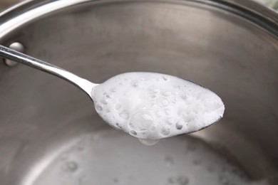 Chemical reaction of vinegar and baking soda in spoon over saucepan, closeup