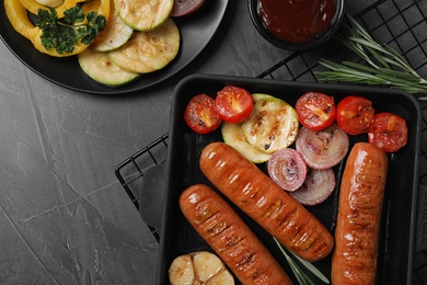 Photo of Delicious grilled sausages and vegetables on grey table, flat lay