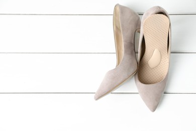 Photo of Orthopedic insoles in high heel shoes on white wooden floor, top view. Space for text
