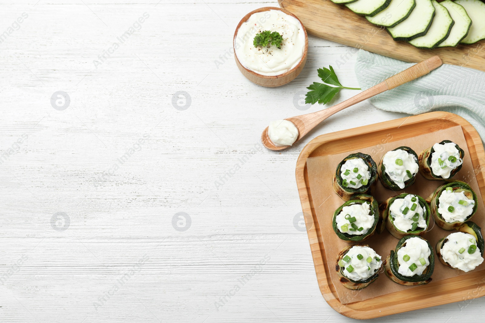 Photo of Stuffed zucchini rolls served with sauce on white wooden table, flat lay. Space for text