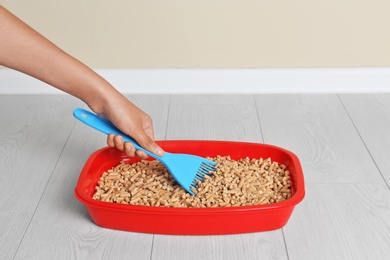 Photo of Woman cleaning cat toilet with scoop on floor. Pet care