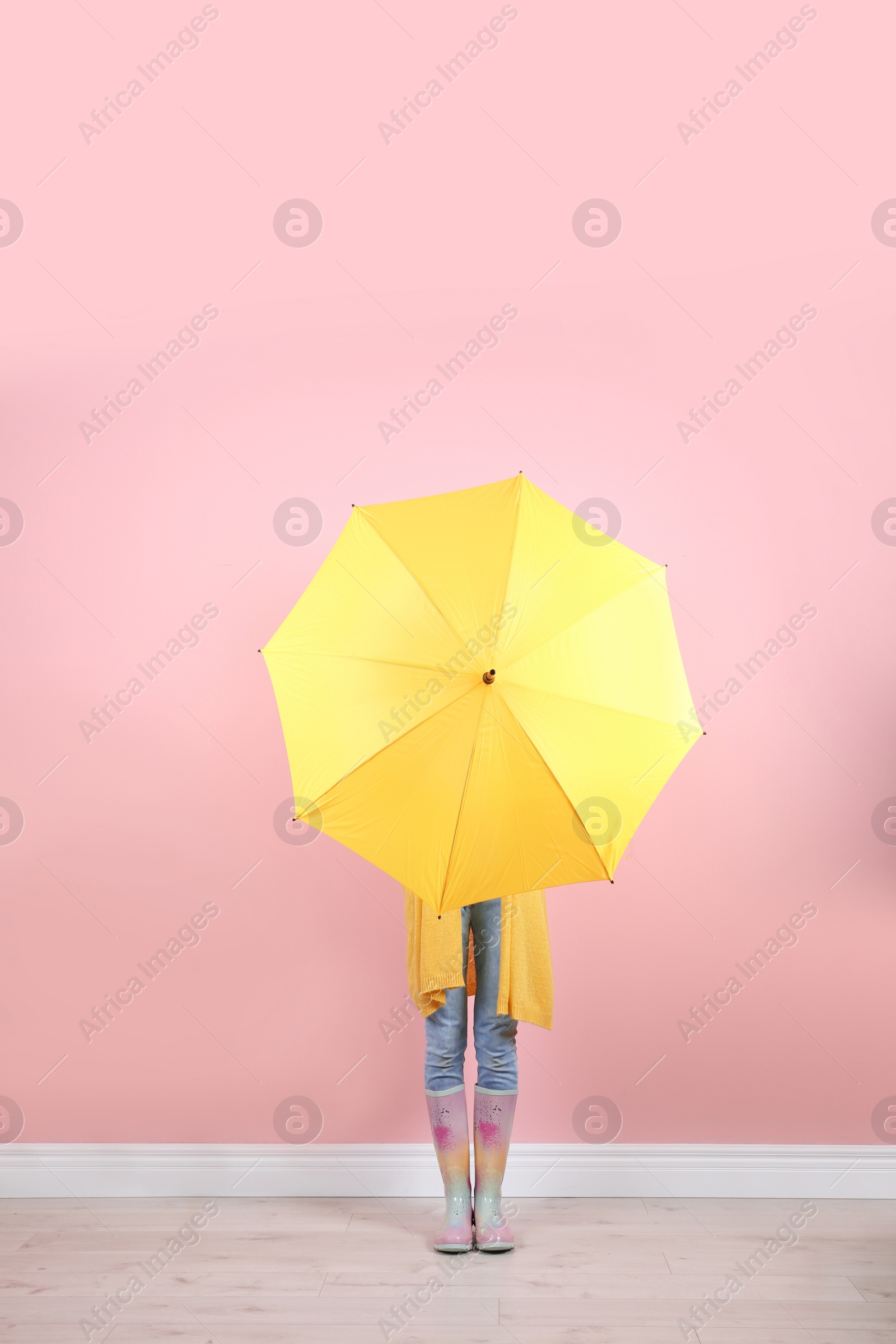 Photo of Woman hiding behind yellow umbrella near color wall