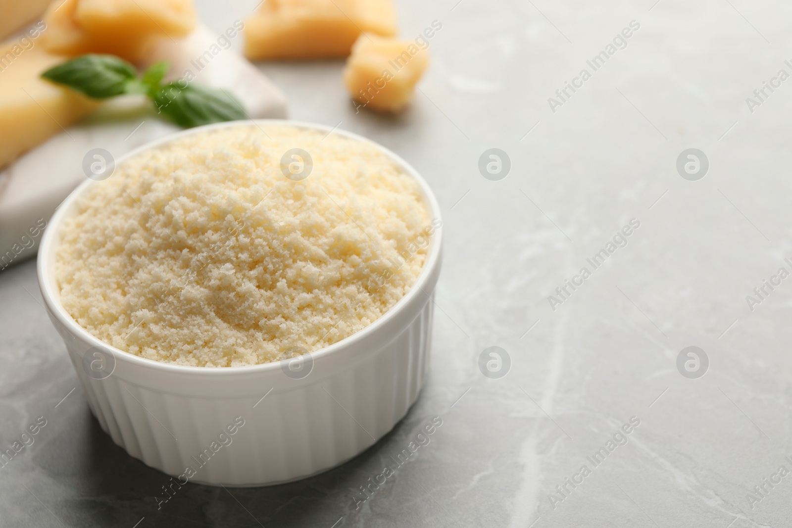 Photo of Bowl with grated parmesan cheese on light marble table, closeup. Space for text