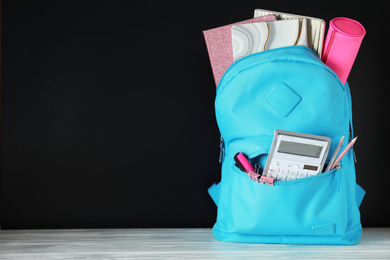 Photo of Bright backpack with school stationery on white wooden table against black background. Space for text