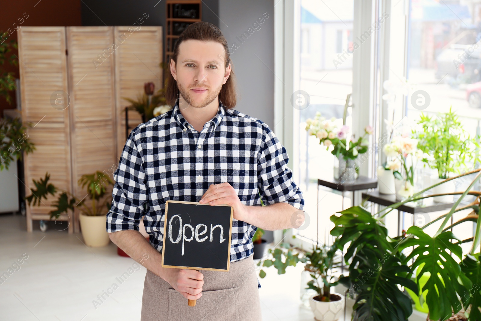 Photo of Male florist holding OPEN sign at workplace