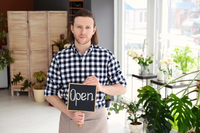 Photo of Male florist holding OPEN sign at workplace