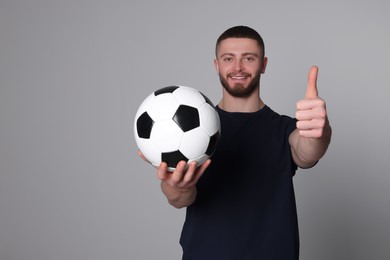 Photo of Athletic young man with soccer ball showing thumb up on light grey background