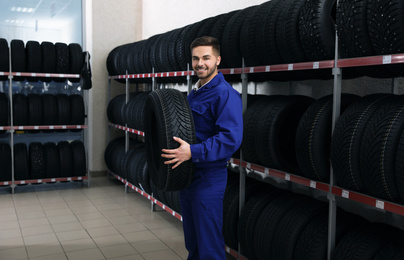 Male mechanic with car tire in auto store